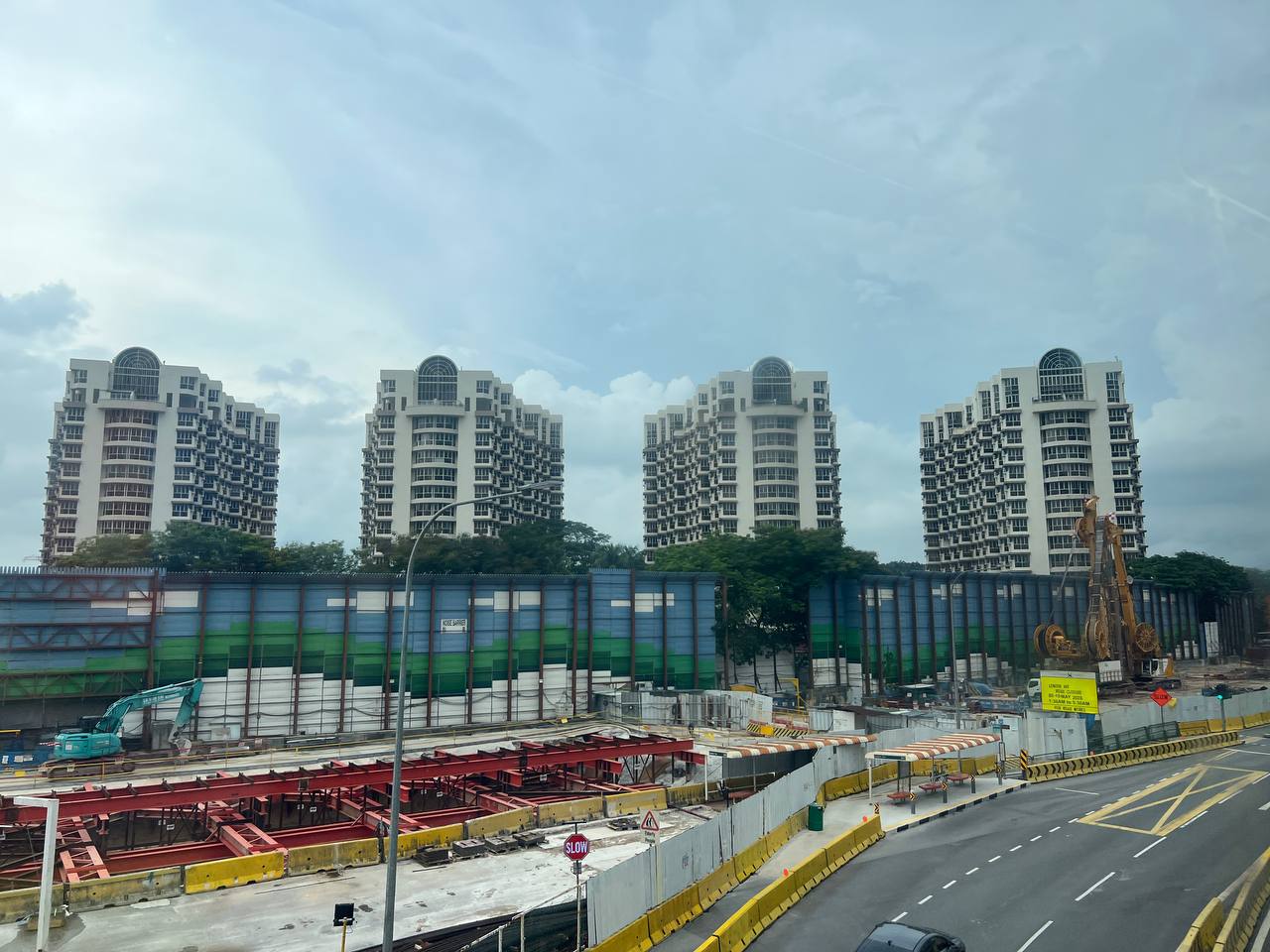 Bullion Park's four towers framed from the Thomson-East Coast Line works site — the new Lentor MRT infrastructure literally being built next to a 472-unit 1993 freehold project. The scale of the development against the new MRT line is the appreciation argument in one image
