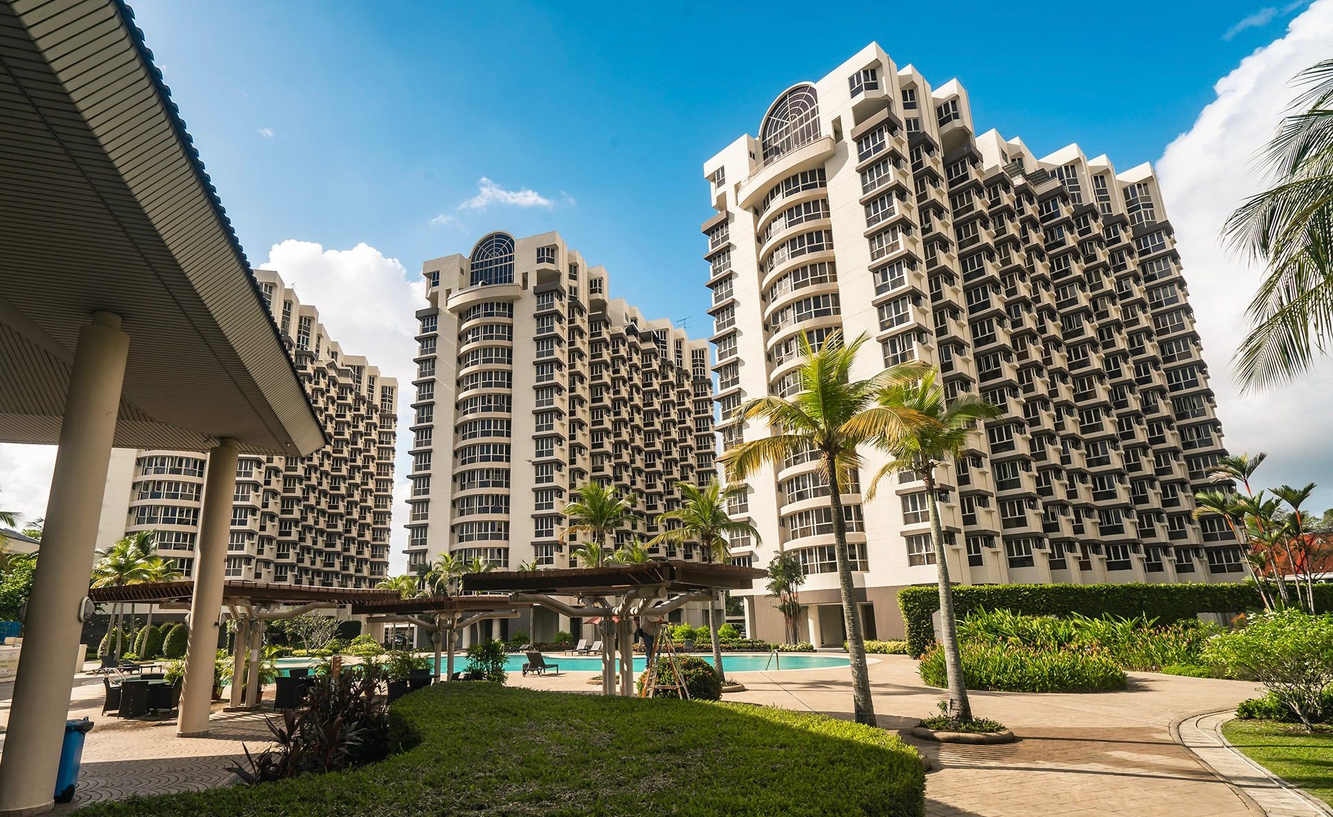 Bullion Park pool deck with the towers behind — three decades of maintained landscaping, palm trees grown to height, an enclave that doesn't feel its age